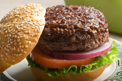 Grilled hamburger with Kaiser bun to the side showing the texture of the meat.  Very shallow DOF.