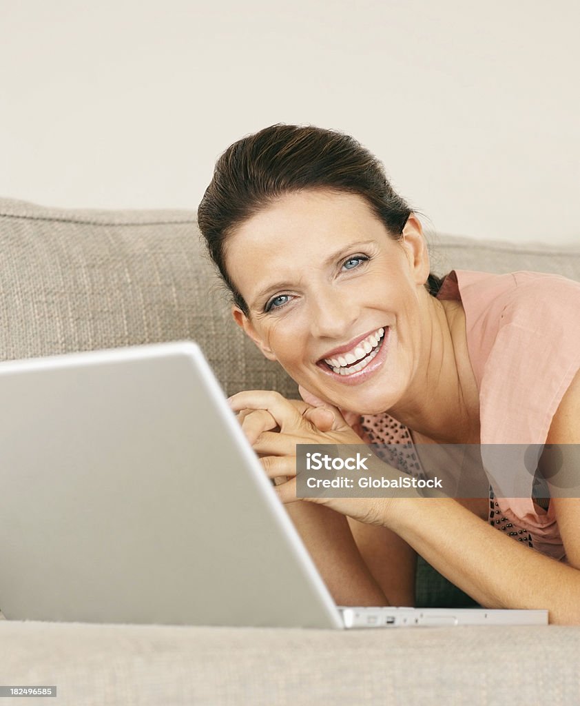 Feliz maturewoman con una computadora portátil en el sofá en casa abajo - Foto de stock de 30-34 años libre de derechos