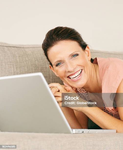 Feliz Maturewoman Con Una Computadora Portátil En El Sofá En Casa Abajo Foto de stock y más banco de imágenes de 30-34 años