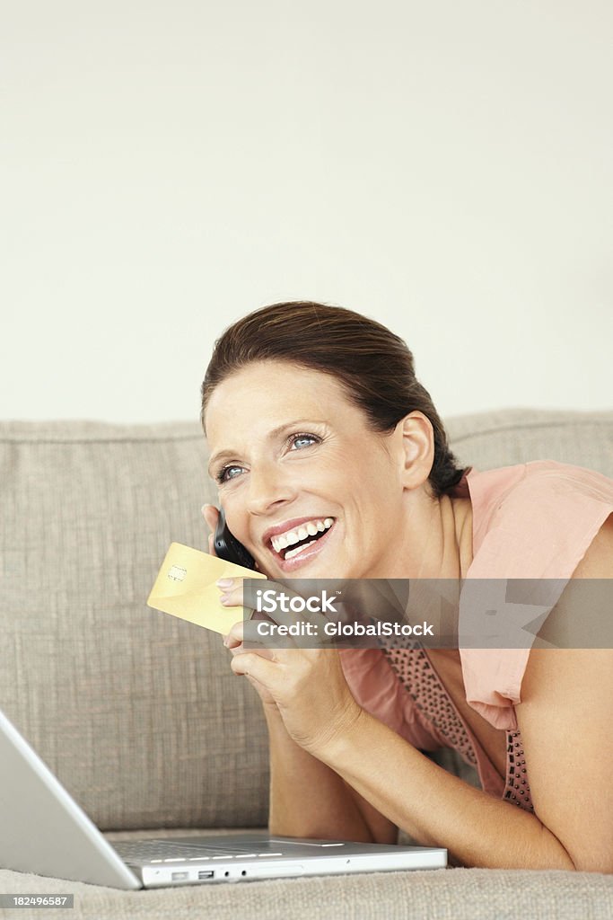 Mujer sonriente con tarjeta de crédito y portátil talking on cellphone - Foto de stock de Acostado boca abajo libre de derechos