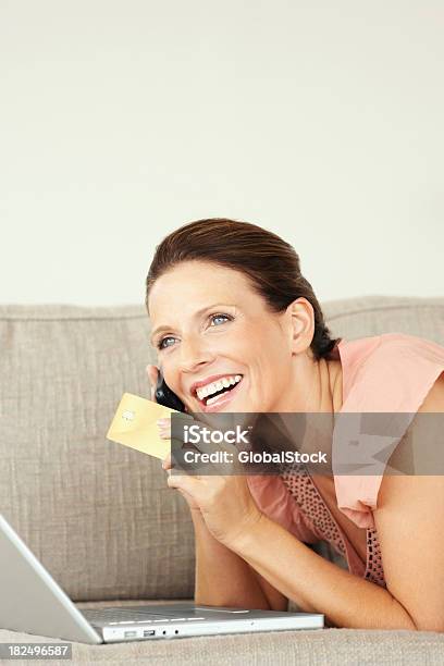 Mujer Sonriente Con Tarjeta De Crédito Y Portátil Talking On Cellphone Foto de stock y más banco de imágenes de Acostado boca abajo