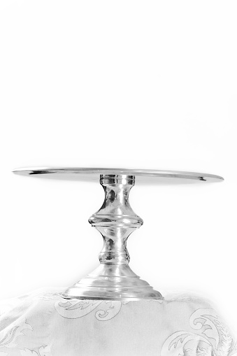 Empty reflective silver cakestand, standing on tablecloth. Isolated on white.
