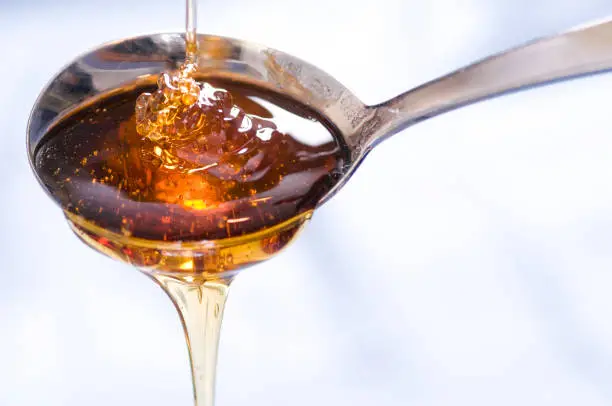 A drizzle of syrup or honey falls into and out of a spoon.