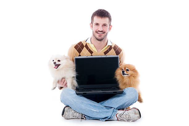 Man Holding a Laptop Computer &amp; Two Pomeranian Dogs stock photo
