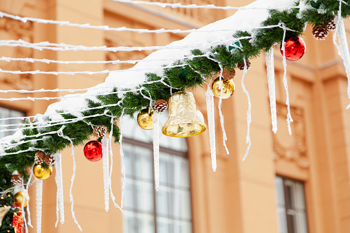 A bell and balls on a garland of fir branches in the snow on the street against the backdrop of classical architecture