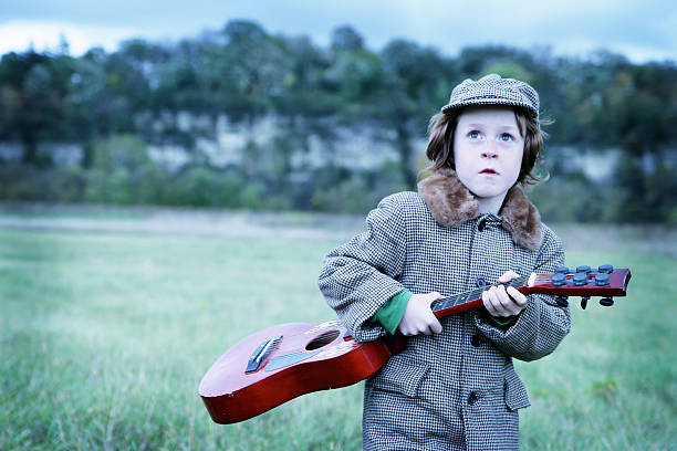 Adorable Little Boy Playing Guitar at Prairie- Alien Invasion! "Adorable little boy in vintage hat and jacket plays red guitar at the prairie. Looks to the sky- aliens!Shot with Canon 1Ds Mark II, cross processed and color saturated, vignette added, copy space." rockabilly boys stock pictures, royalty-free photos & images