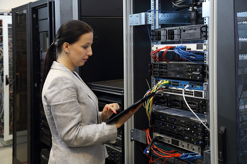 Woman in data center programing mainframe on a digital tablet.