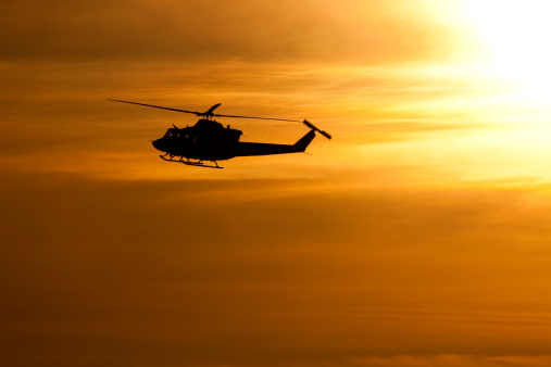 The silhouette of a helicopter against a setting sun.  Engine exhaust vapors can be seen pouring from the back.