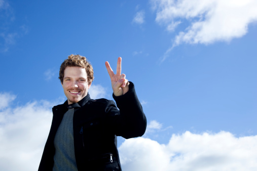 smiling man making the peace sign against blue sky