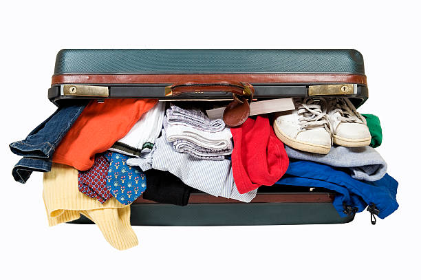 An open suitcase with clothes and shoes falling out of it stock photo
