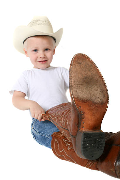 Cowboy cutie in t-shirt and jeans pulls on fathers boots stock photo