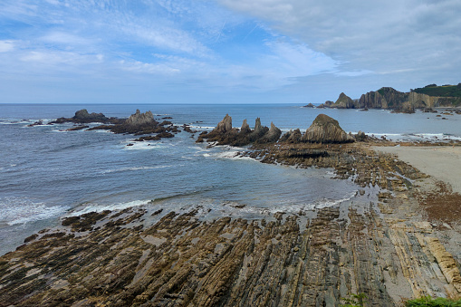 rocky beach with jagged rocks and cliffs in the background, taken on a day with a light blue sky