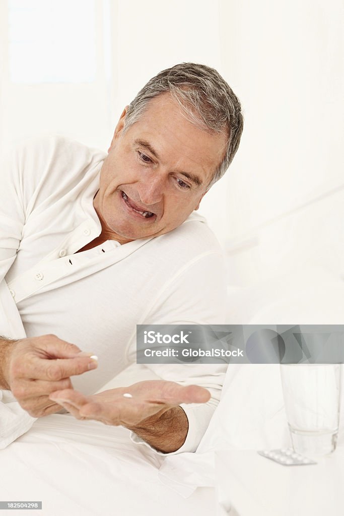 Elderly man taking medication before sleep Unhappy senior man on bed taking his medication before sleep 60-69 Years Stock Photo