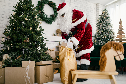 An African American man in Santa costume representing for the Christmas holiday silently delivers gifts and presents under the tree.