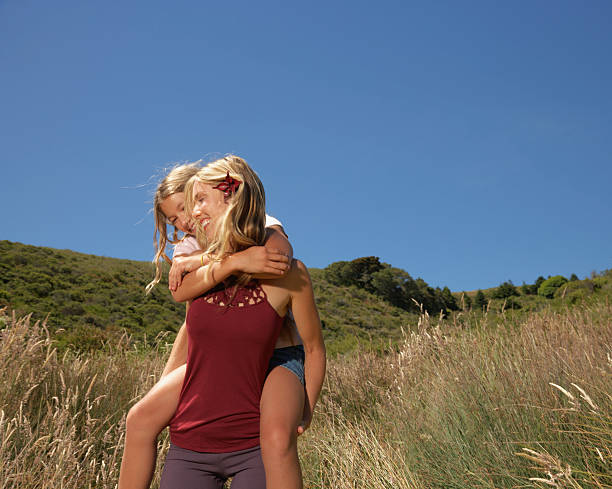 Mother Giving Daughter Piggy-Back Ride in Meadow stock photo