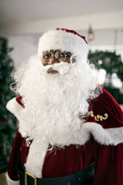 An African American man in Santa costume representing for the Christmas holiday.  Shot in a festive room with Christmas decorations.