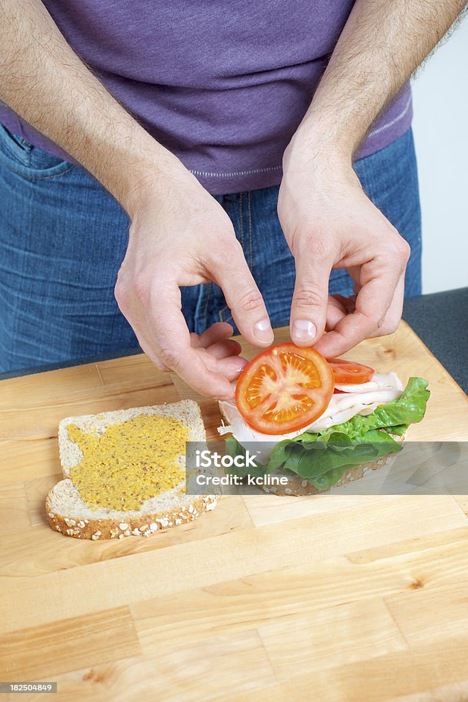 Making a Sandwich A man's hands putting tomato slices on a turkey sandwich. Adult Stock Photo