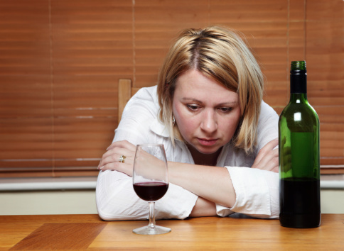 Depressed and thoughtful looking woman in her forties turns to alcohol for comfort. Shallow DOF, focus on hand