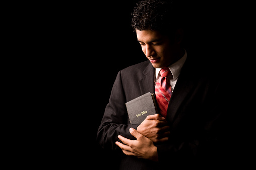 Young man holding a Bible and posing on a black background