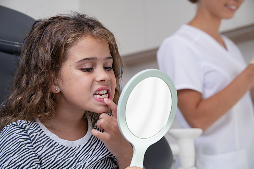 Portrait of a girl being examined by a dentist in a dental chair. The girl is looking in the double-sided mirror checking the appearance of his teeth after the dentist's intervention.