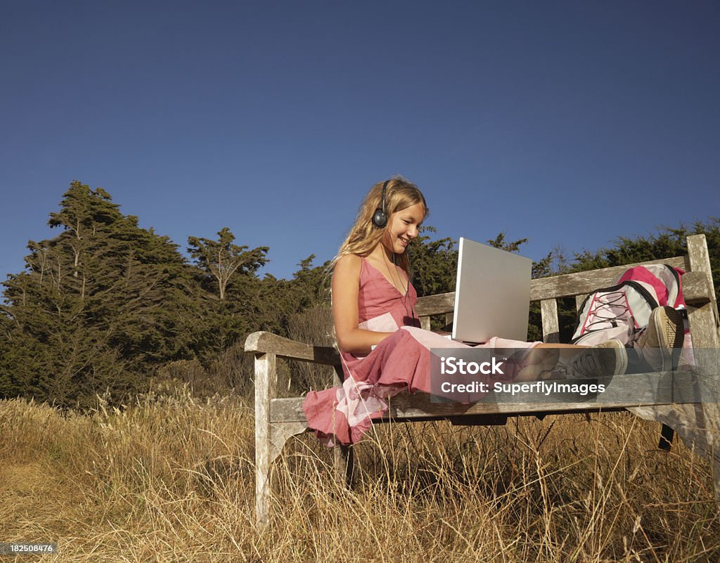 Teen sorridente no banco com computador portátil e auscultadores - Royalty-free Ler Foto de stock