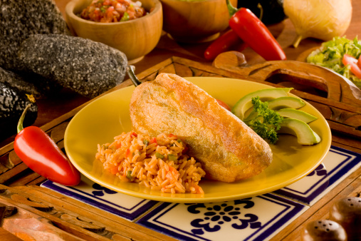 Chile Relleno or Poblano Pepper stuffed with beef and served with rice and avocado on Mexican ambience