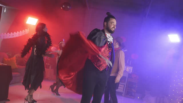 Man in a costume with a cape dancing and smiling at camera during a Halloween party