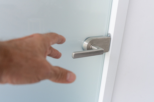 The hand of an old man grasps a handle on a sandblasted glass door