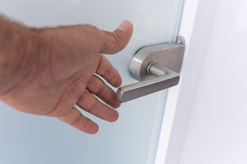 The hand of an old man grasps a handle on a sandblasted glass door