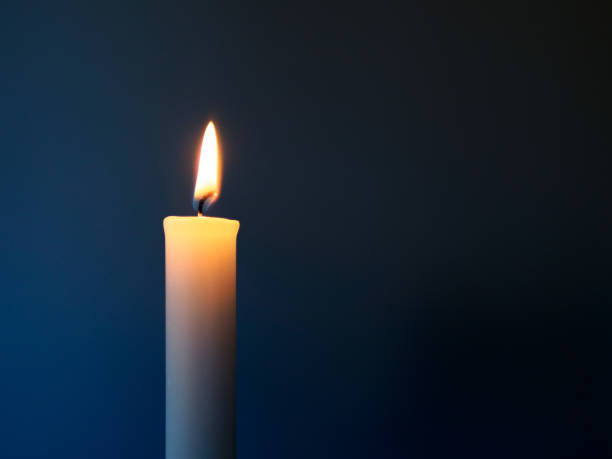 Burning white candle in front of a dark blue background