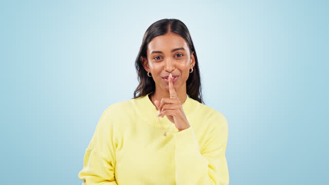 Secret, woman and face in studio with fashion, gossip and confidential news with blue background. Smile, silence sign and female person from India with a portrait and quiet voice for announcement