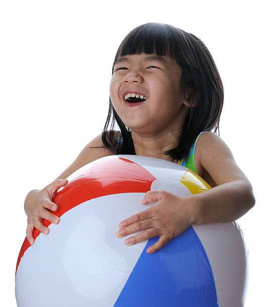 A little girl laughs while holding onto a colorful beach ball.