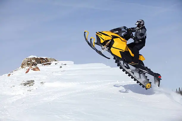 Snowmobile jumping as he tops the mountion.