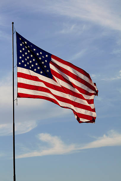 istock American Flag against pale blue sky with clouds 182511423
