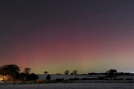 Green and red Northern Lights above snow covered fields in Northumberland