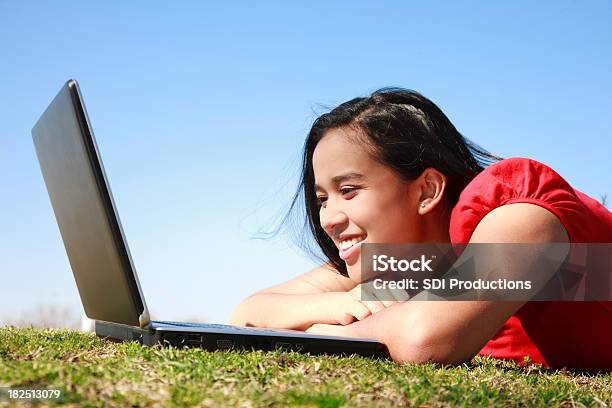 Giovane Donna Guardando Un Computer Portatile Sullerba - Fotografie stock e altre immagini di Abbigliamento casual