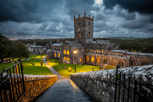 Moody clouds over St David's Cathedral in Pembrokeshire, Wales. The warm light of the illuminated windows are in beautiful contrast to the bluish cloudscape and landscape at dusk time. Wales - UK