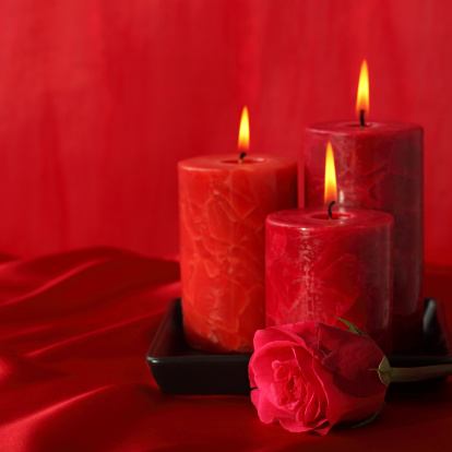 Burning red candles and rose on red background