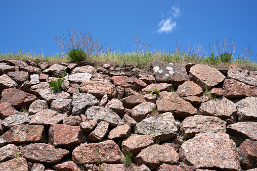 Close-up of ancient red granite stone brick wall, blue clean sky, green grass