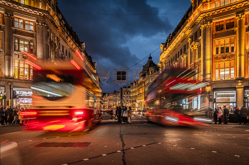 Traffic and crowds of people at Oxford Circus in London. Buildings on Oxford streets are already illuminated under a moody dusk sky. London,England, UK