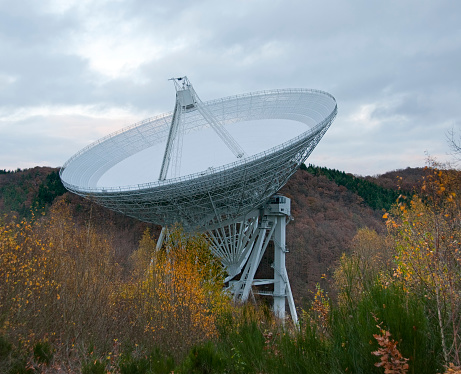 An  astronomic telescope located in a remote valley, surrounded by hills, trees an bushes. Moody overcast sky.