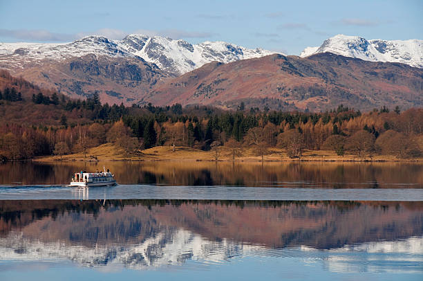 Lake Windermere Winter "Small tourist boat cuts its way through a covering of ice on Lake Windermere. Langdale pikes, covered in snow, reflected in calm waters." langdale pikes stock pictures, royalty-free photos & images