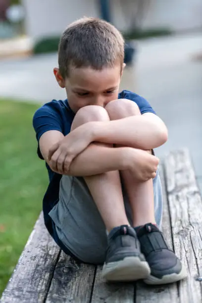 Photo of Crestfallen Crying child boy sitting at the schoolyard covering his face