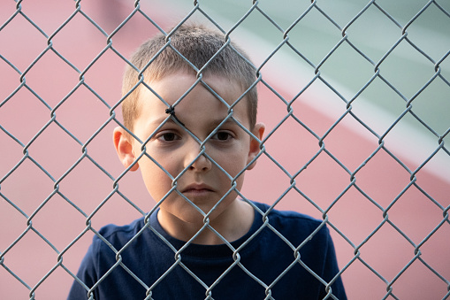 Sad little boy looking through a fence