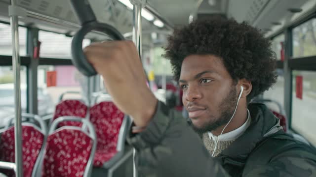 While looking through the bus window, male passenger Black ethnicity, listening to music on headphones
