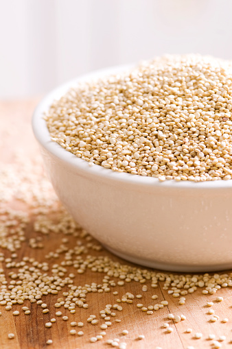 A bowl of raw, uncooked quinoa on a rough wooden surface.