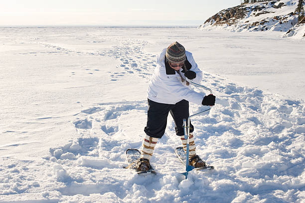 A woman drills a hole in the ice with an ice auger on Great Slave Lake in Canada's Arctic to begin ice fishing.  Click to view similar images.