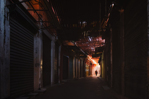 Diminishing perspective of a distant lone silhouette of a local man walking through the dark souks of the Marrakech medina early morning before the shops open.