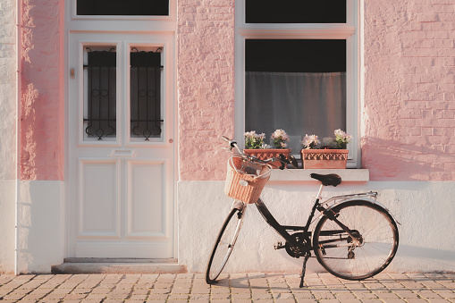 Vintage still life scene of a bicycle parked outside of quaint pastel pink home exterior along a quiet lane on a Spring day in the old town of Bruges, Belgium.