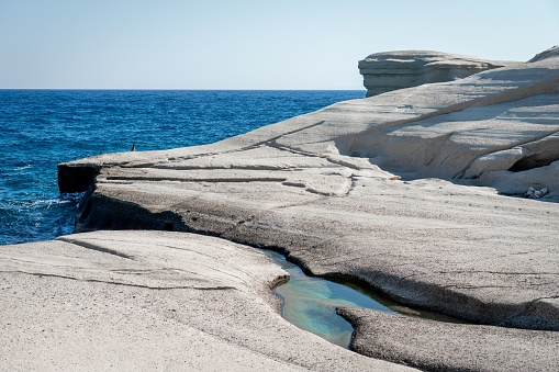 A scenic landscape with a large rock face surrounded by crystal-clear water, featuring small bubbles floating atop the surface